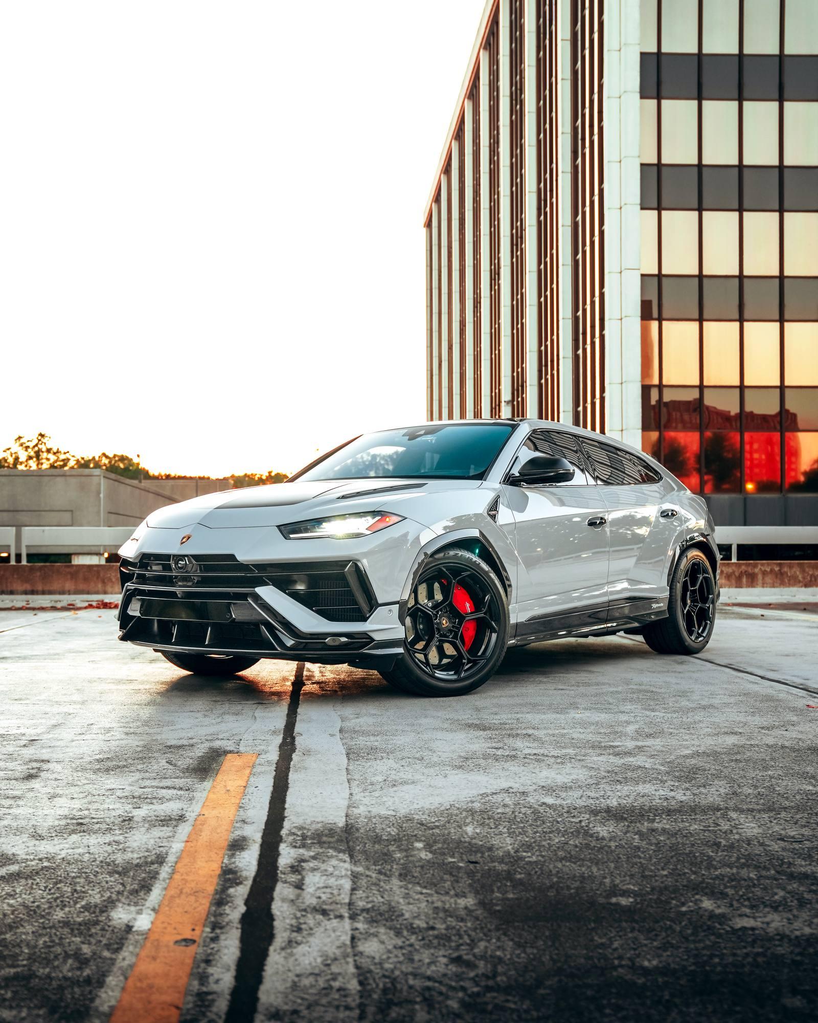 Silver Lamborghini Urus with tinted glass in front of an office tower at sunset